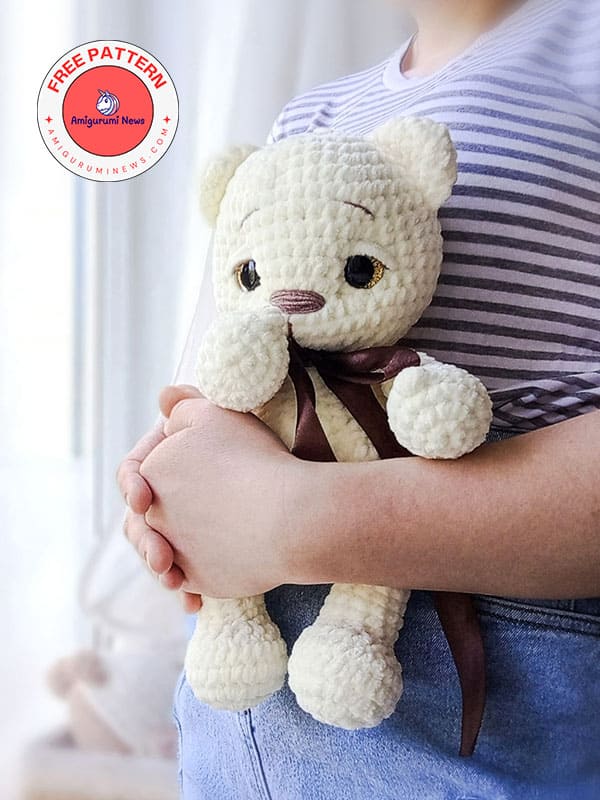 Child holding a handmade cream-colored crochet teddy bear with brown ribbon.